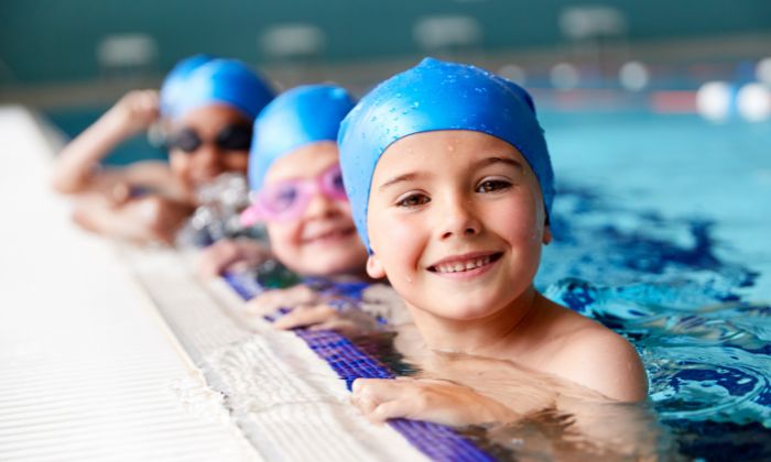 Vier Kinder in einem Schwimmbecken halten sich am Rand des Beckens fest.